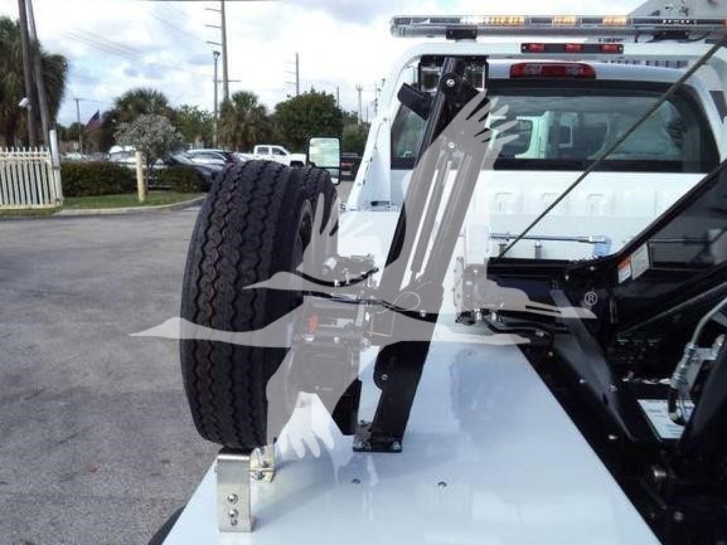 Trucks equipment showing rear view of a white 2023 Chevrolet Silverado 6500HD with a mounted winch and spare tire on the back, highway in background.