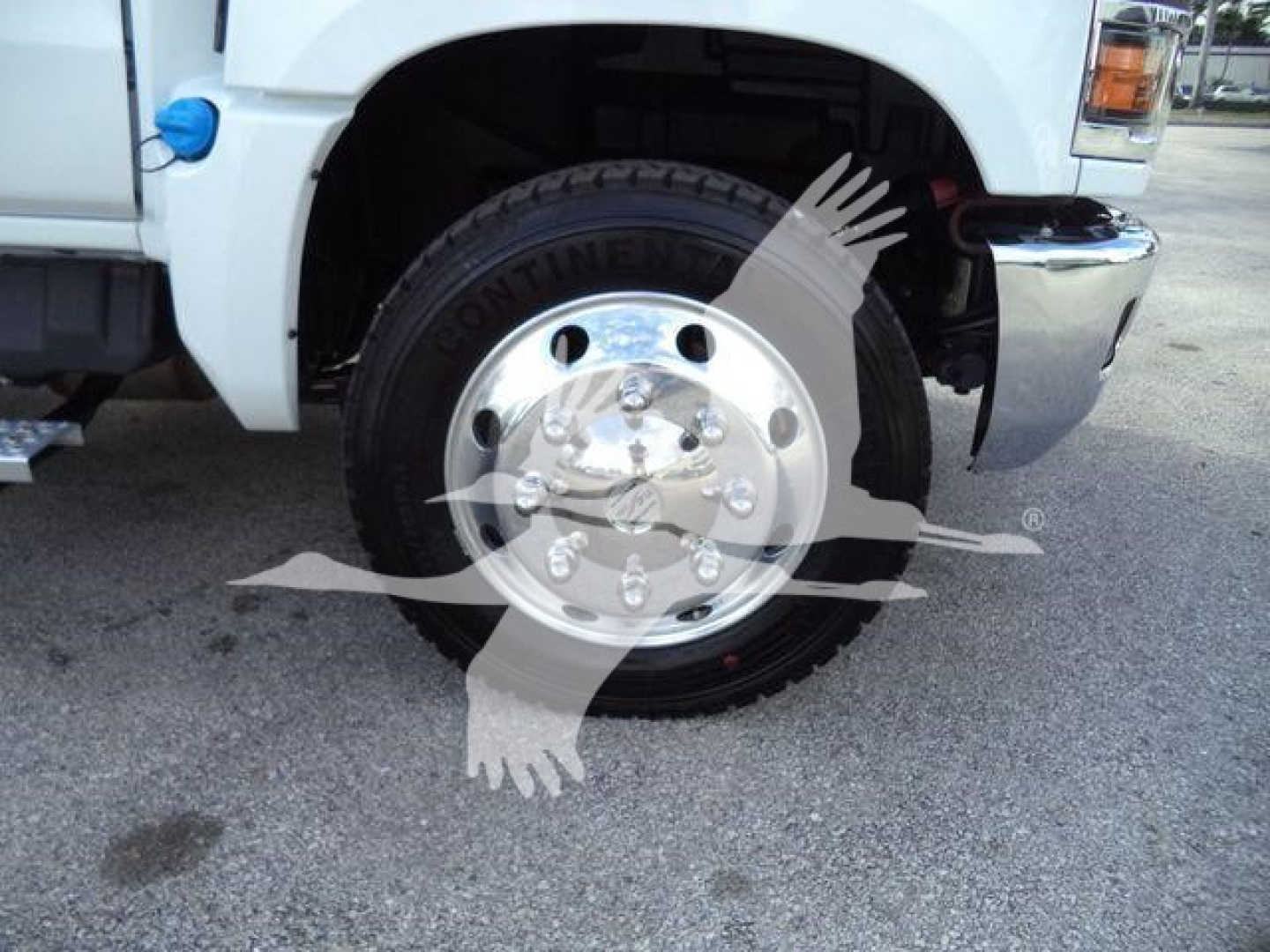 Front left wheel of a white Chevrolet Silverado 6500HD truck showing Continen tal tire and chrome wheel with vehicle fender and bumper.