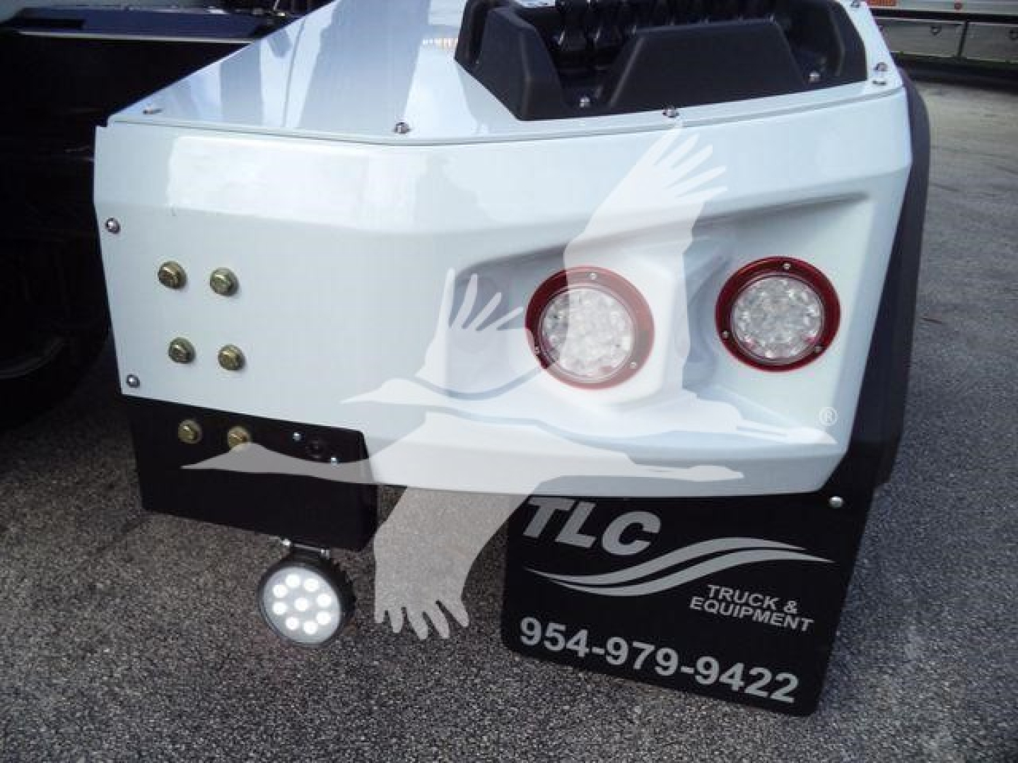 Back of white Chevy Silverado 6500HD winch truck bed showing two round taillights, LED work light, and TLC Truck & Equipment logo with phone number 954-979-9422.