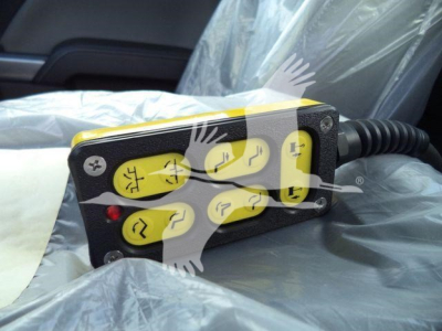 Control pendant with multiple yellow buttons and black housing, connected by a coiled cable, mounted on a vehicle seat.