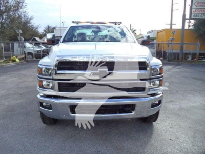 Front view of a white 2023 Chevrolet Silverado 6500HD truck with chrome grille, bumper, and dual headlights in a lot.