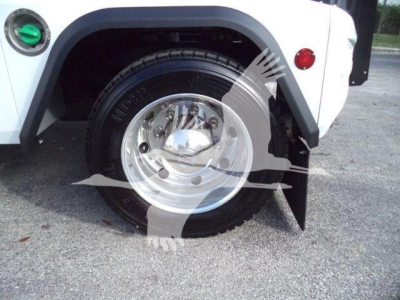 Front wheel and fender of a white Chevrolet Silverado 6500HD, showing a polished wheel, black tire, fender flare, and a green circular fuel cap on the left.