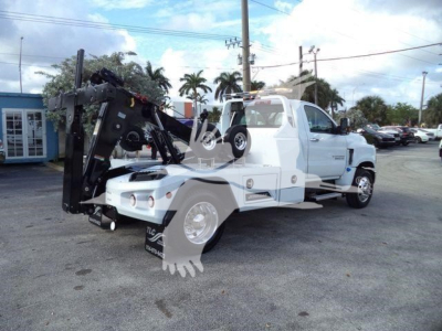 2023 Chevrolet Silverado 6500HD wrecker/utility truck with crane arm and flatbed, front angled view showing white cab and black towing equipment.