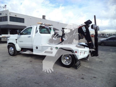 Truck-mounted recovery wrecker on a white 2023 Chevrolet Silverado 6500HD with a hydraulic boom and winch in a dealership lot.
