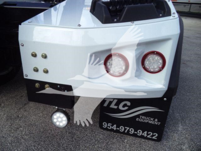 Back of white Chevy Silverado 6500HD winch truck bed showing two round taillights, LED work light, and TLC Truck & Equipment logo with phone number 954-979-9422.