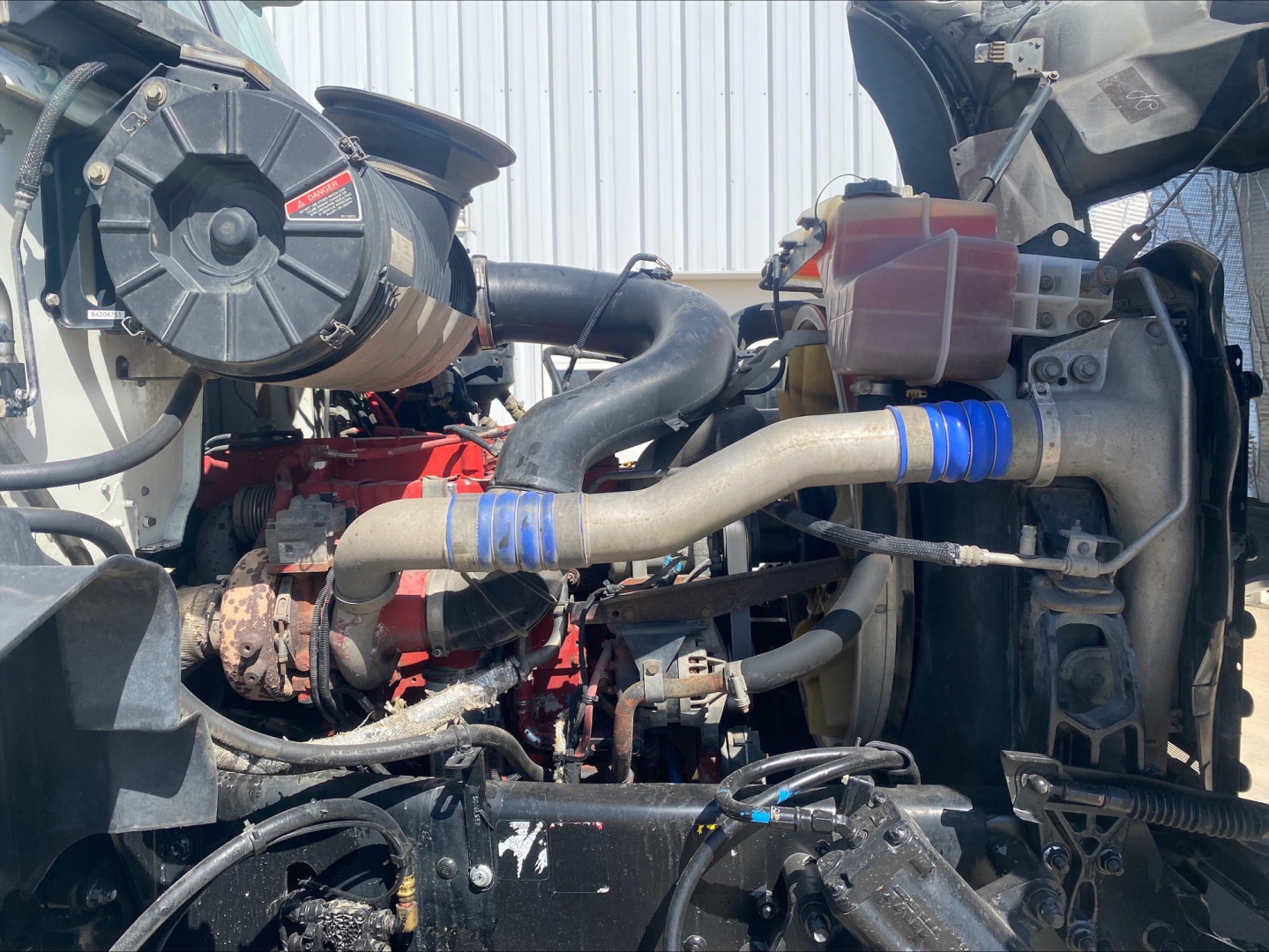 Engine bay of a 2018 Mack GU533 with visible intake hose, red engine block, coolant reservoir, belts, and various hoses.