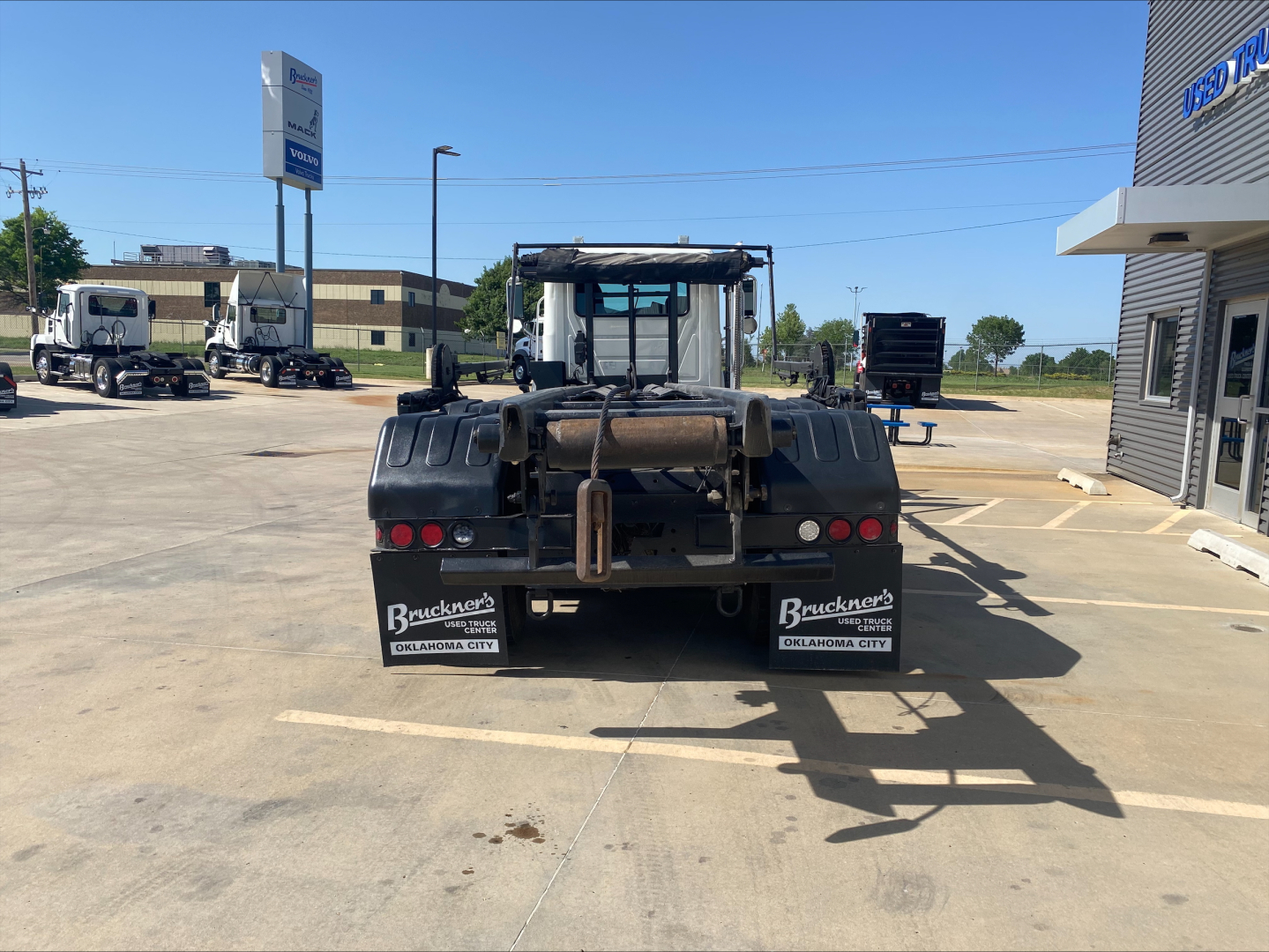 Rear view of a 2018 Mack GU533 roll-off truck showing towing hitch, bumper, taillights, and mudflaps with Buckner's logo. Stock plates and dealership signage visible.