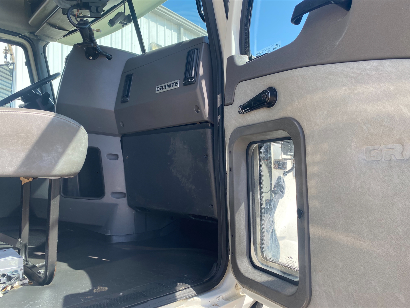 Cab interior of a Mack GU533 showing the driver's seat, dashboard with a label reading GRANITE, and a side door with a window.