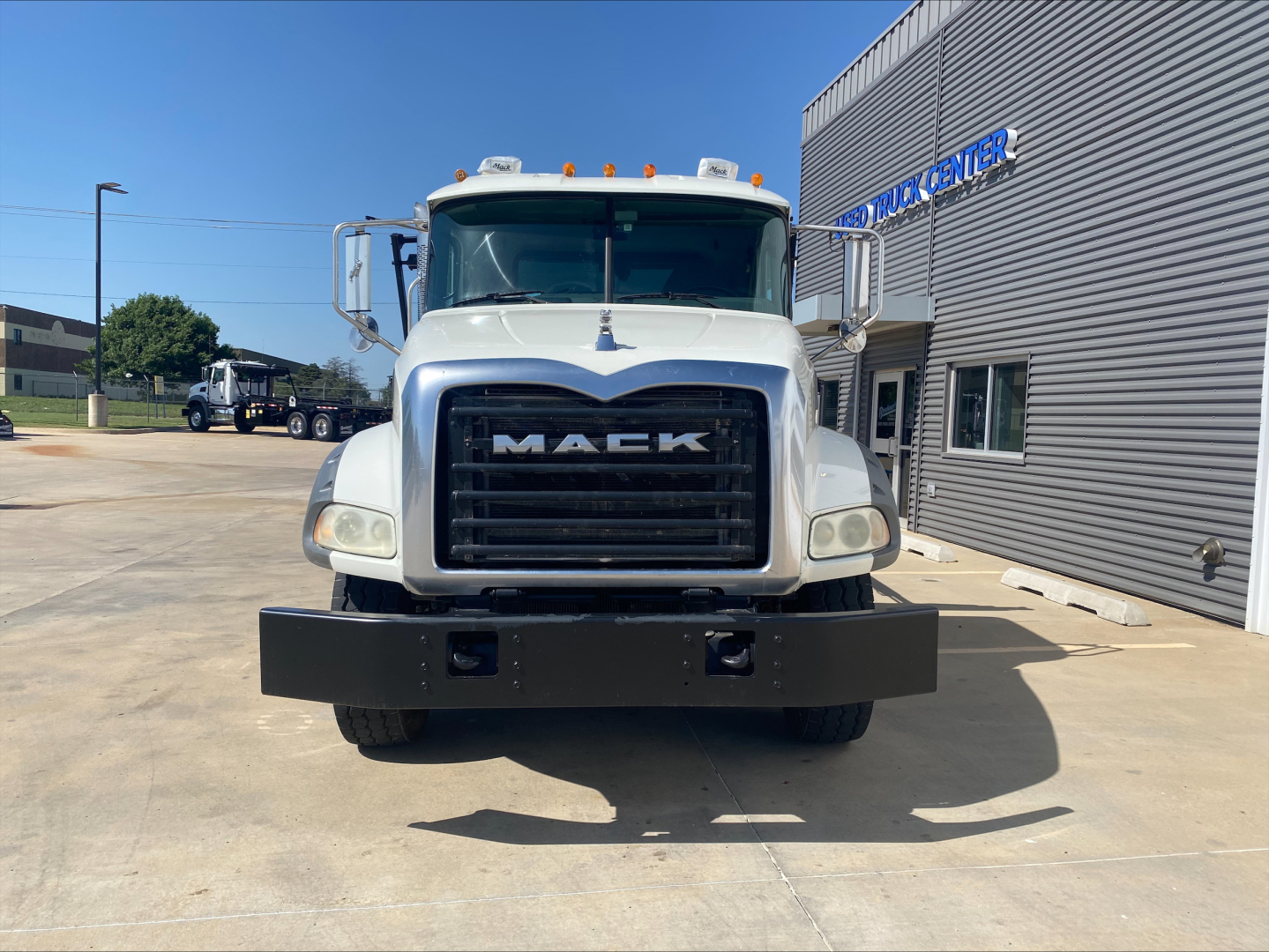 Mack GU533 front view showing large black grille with MAC K letters, white cab, bumper with two recessed lights, dealership building in background.