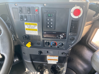 Dashboard view of 2018 Mack GU533 roll-off truck cab showing control switches, warning labels, gear selector, and climate controls.