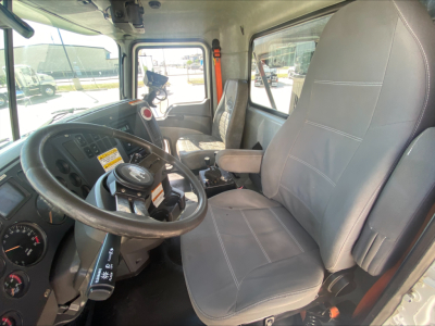 Cab interior of a 2018 Mack GU533 roll-off truck showing steering wheel, instrument cluster, gray fabric seats, and control levers.