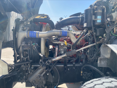 Mack GU533 engine bay view showing connected hoses, turbo, and intake piping in front of the cab; various metal brackets and hydraulic lines visible.