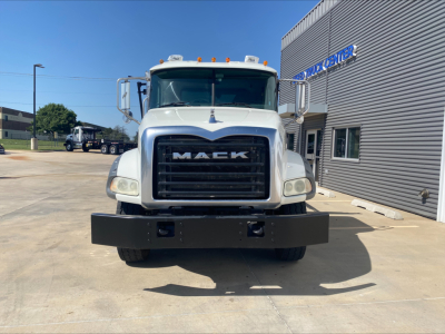 Mack GU533 front view showing large black grille with MAC K letters, white cab, bumper with two recessed lights, dealership building in background.