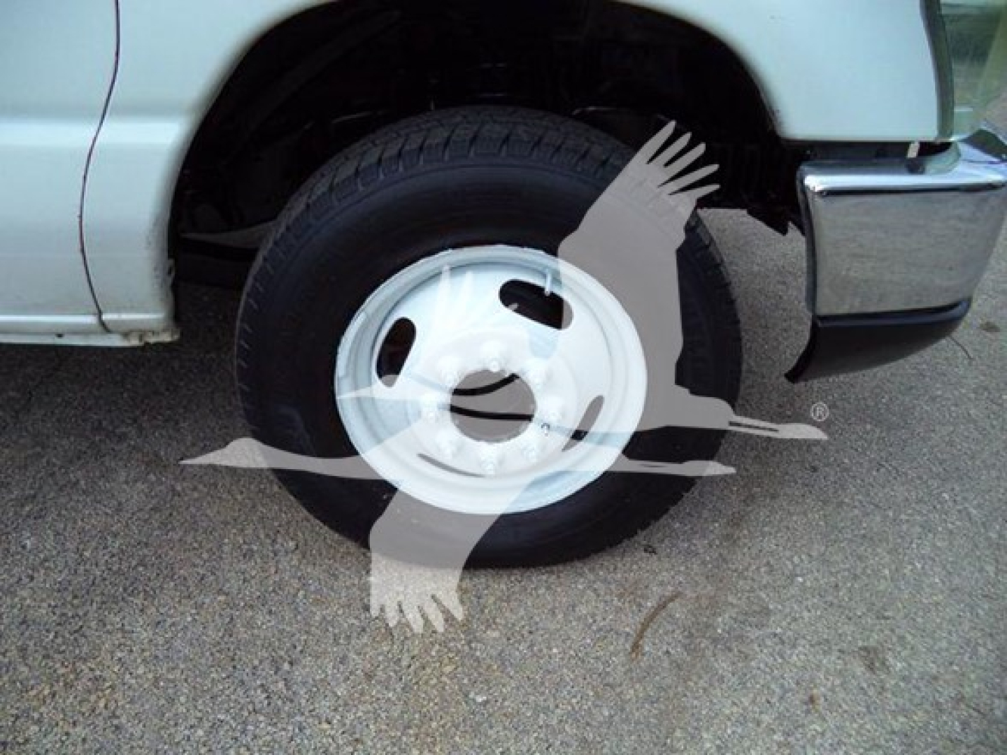 Ford E-Series front left wheel and fender showing hub and tire; partial front bumper visible.