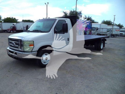 Ford E-Series flatbed truck in a used lot showing front grille and flatbed cargo area.