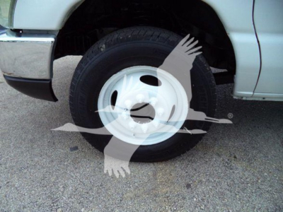 Ford E450 wheel and tire visible in the wheel well of a gray truck, front-left side, white steel wheel.