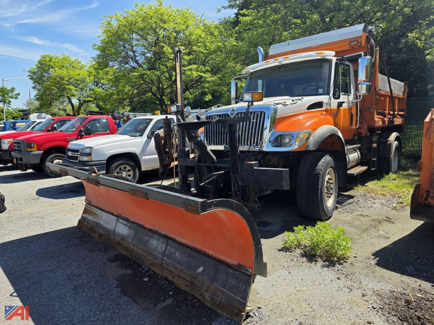 Dump truck with plow and sander body showing large orange snow plow attachment in front and an orange and white cab, International WorkStar 7400, parked in lot.