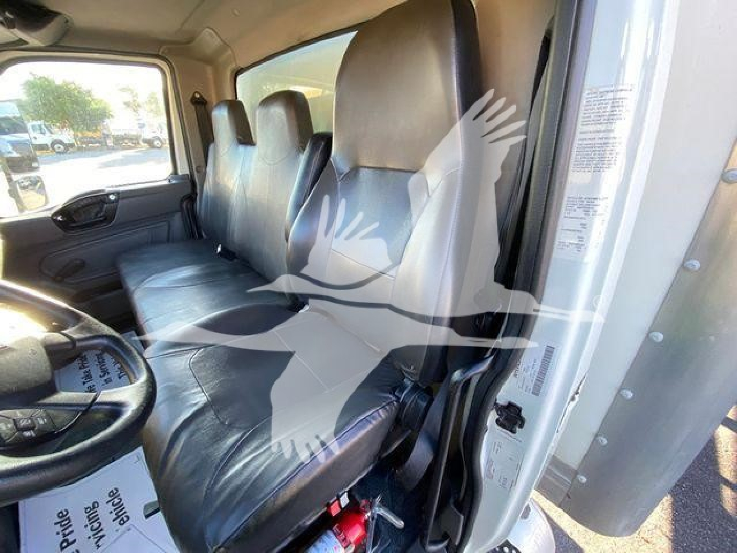 Truck interior showing front bench seats and part of the driver side with seat belt. Visible text on door frame labels and window sticker.