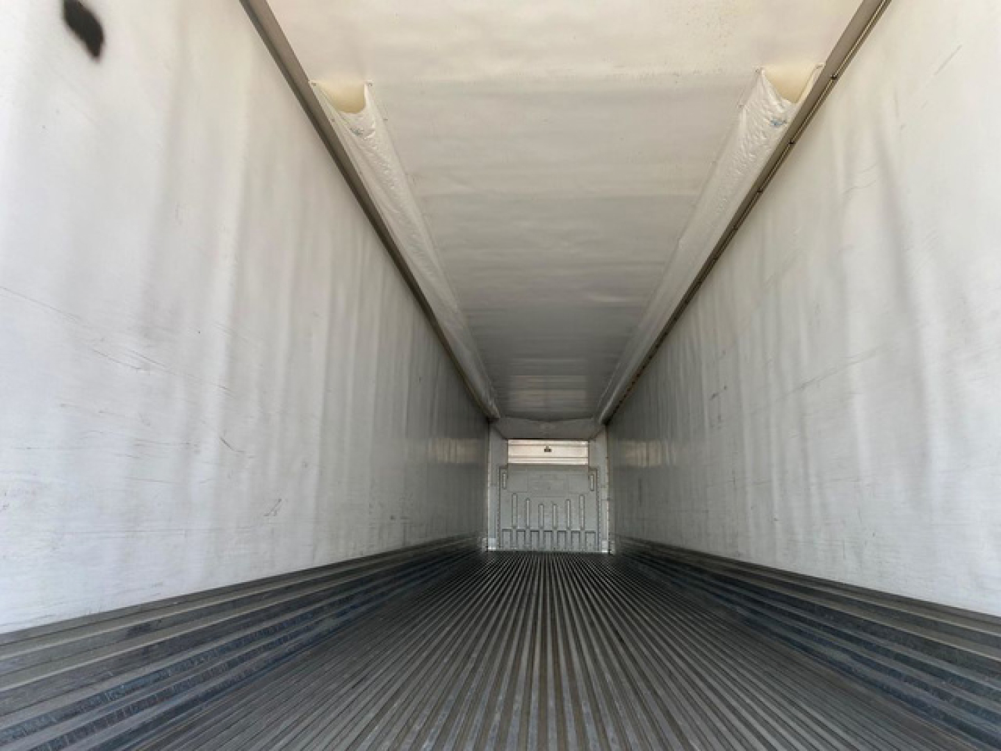 Trailer interior showing white refrigerated container with corrugated metal floor and side walls, leading to rear door, no visible markings