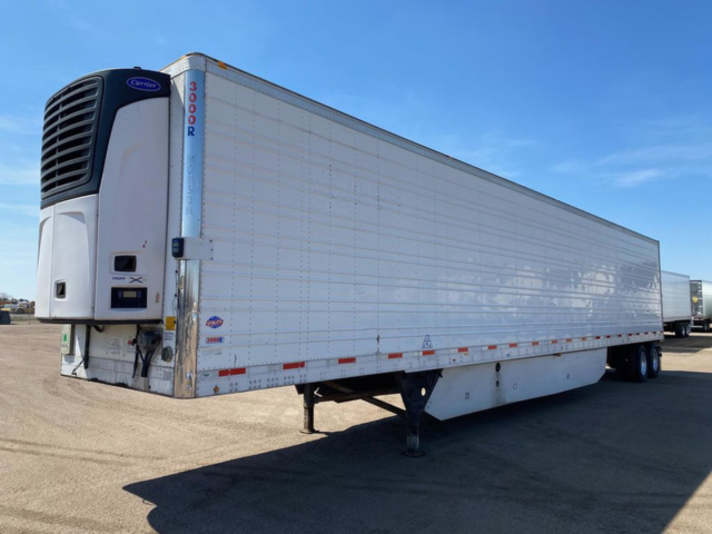Trailer with a Utility reefer unit on front left; white refrigerated semi-trailer with blue Thermo King/Carrier reefer unit, raised landing gear, side markers, and regulatory decals visible.