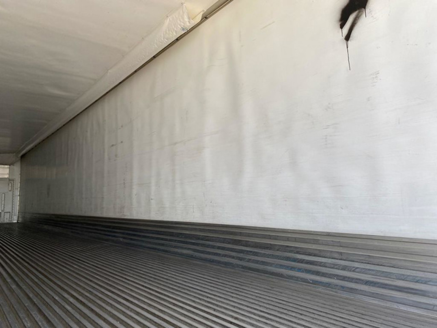 Utility reefer trailer interior cargo area with ribbed floor and blank insulated walls, empty bay for loading.