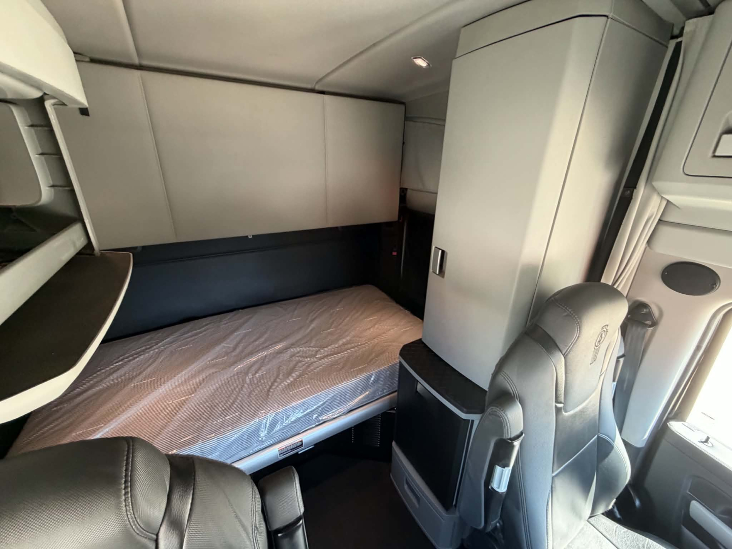 Truck cab interior of a 2022 Kenworth T680 sleeper showing bunk bed and storage cabinet.