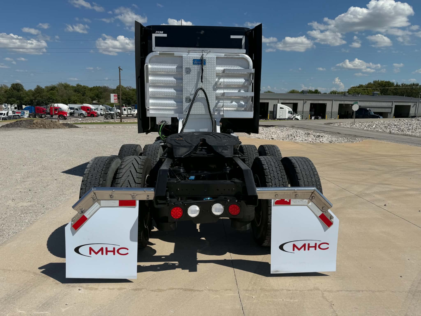 Kenworth T680 rear view showing fifth wheel, dual rear axles, and white MHC mudflaps with red logos.