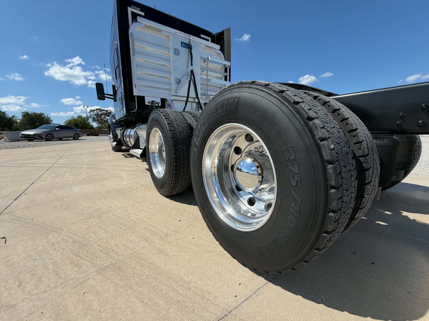 Kenworth T680 truck chassis with dual rear wheels and a metal toolbox. Visible text includes tire sidewall markings: 275/80R. Clear blue sky.