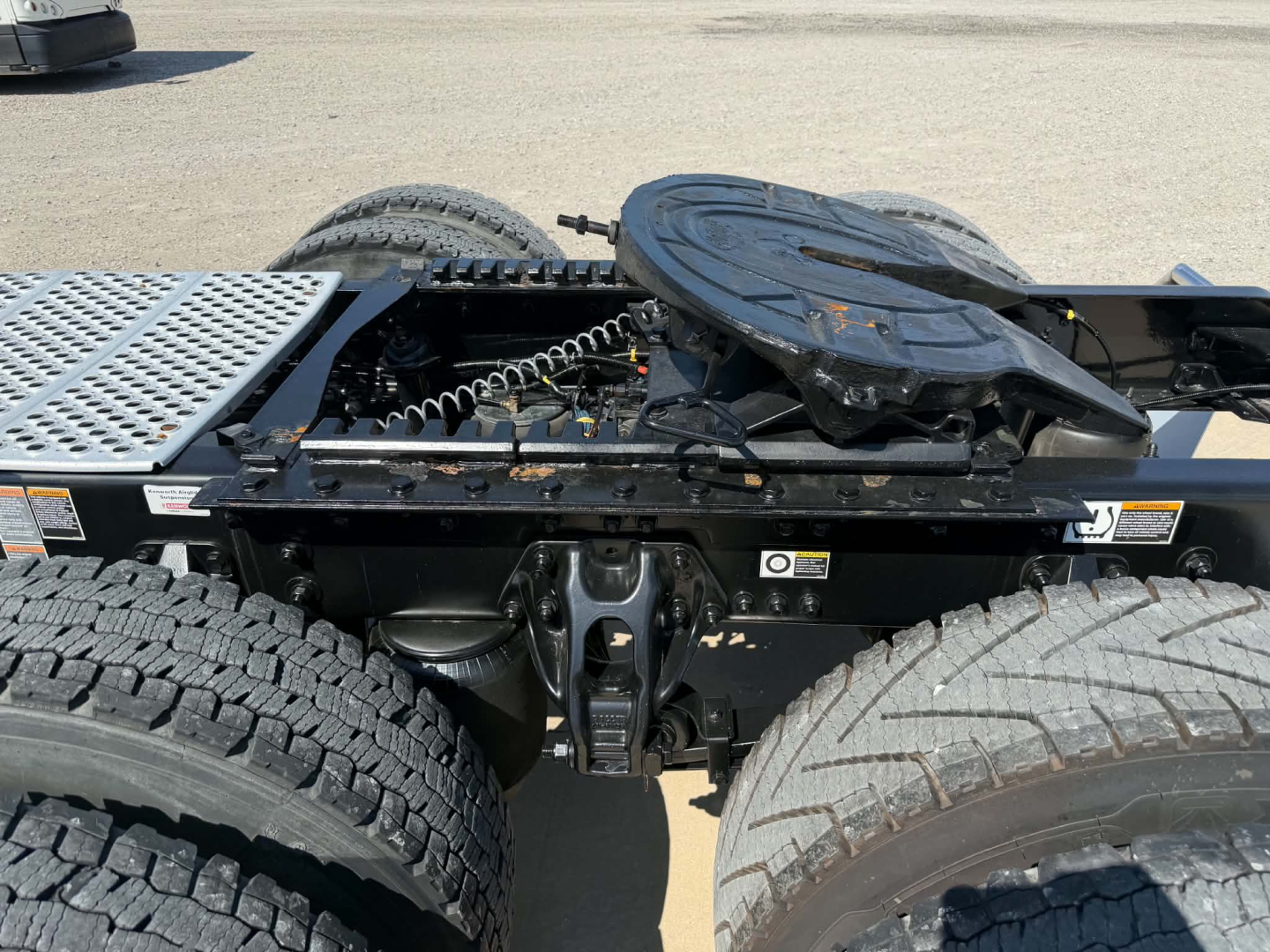 Kenworth T680 tractor cab chassis showing fifth wheel and rear axle area with spare tire mount and drivetrain components visible.