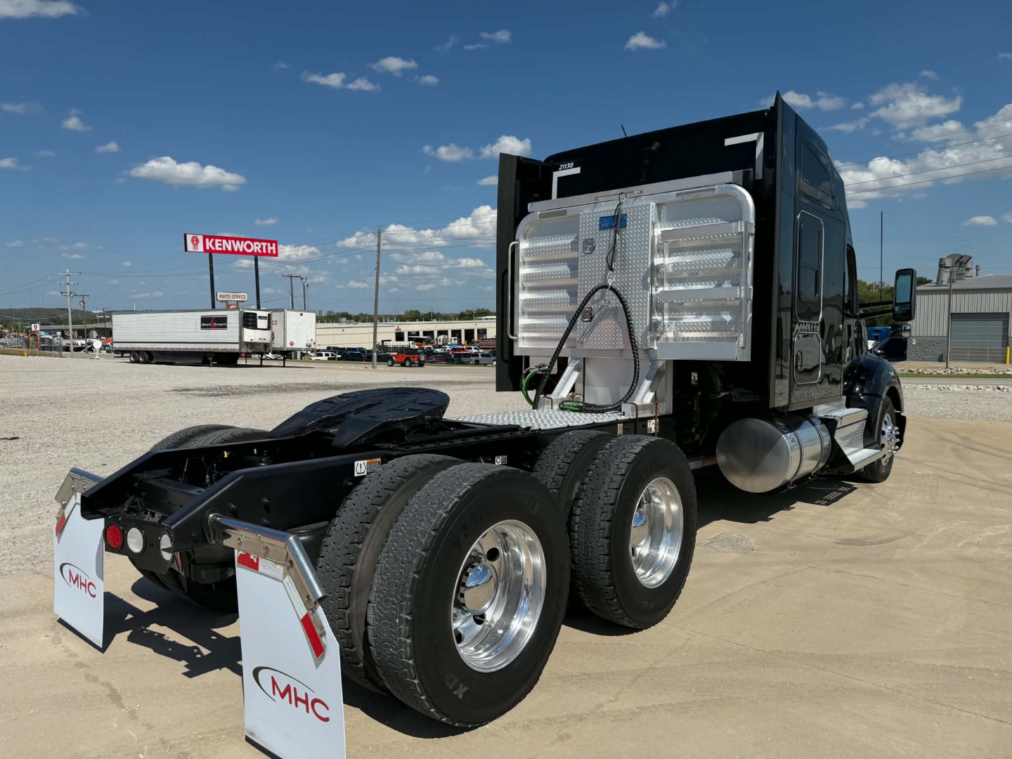 Kenworth T680 tractor tractor cab and dual rear axles in a truck yard with chrome metal fuel tank and trailer hitch area visible.