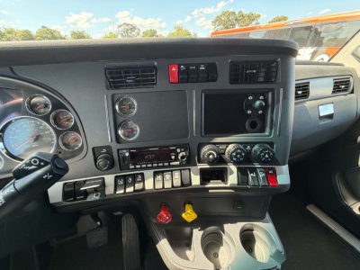 Kenworth T680 cab interior view showing dashboard gauges, switches, and center console with two cup holders and knobs.