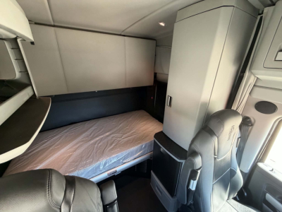 Truck cab interior of a 2022 Kenworth T680 sleeper showing bunk bed and storage cabinet.