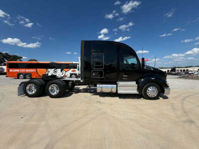 Kenworth T680 cab with black exterior and chrome fuel tanks on a dirt lot. Side trailer shows orange and white Oklahoma State University graphic and mascot image.