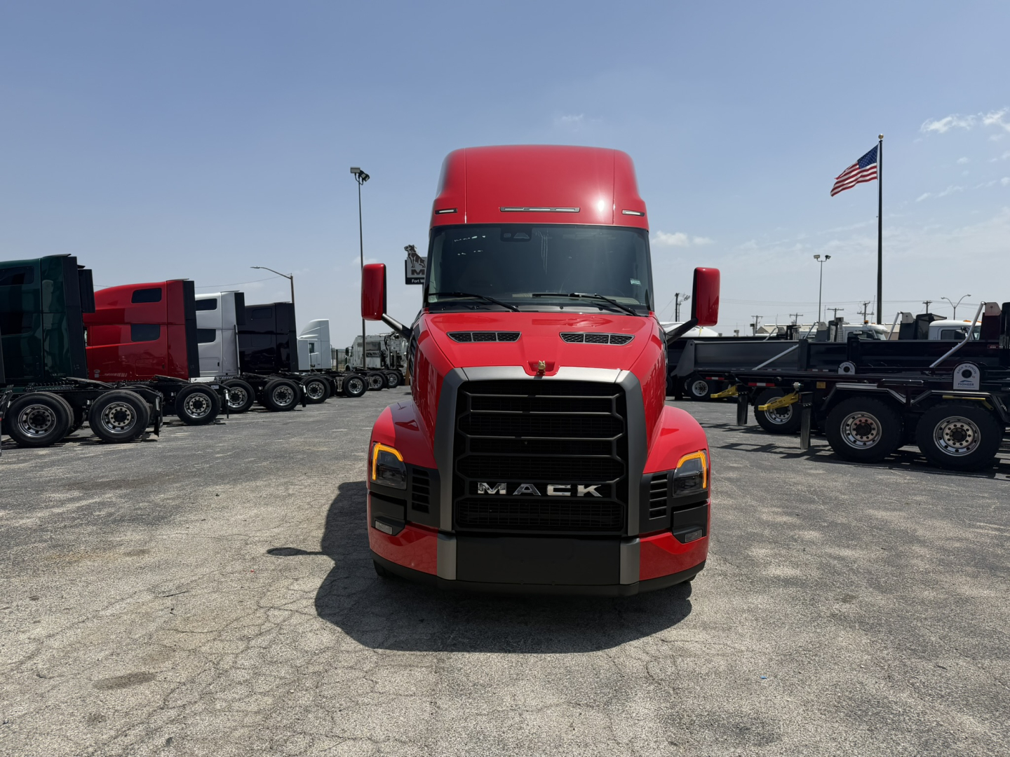 Front view of a red 2027 Mack PR64T76H truck showing bold black grille and headlights in a truck lot.