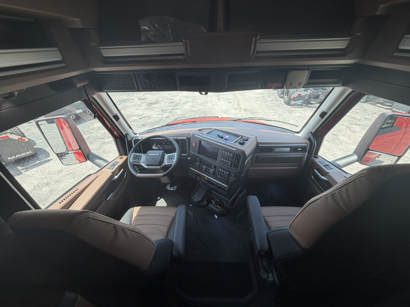 Interior cab of a new Mack PR64T76H truck showing steering wheel, dashboard with controls, two front seats, and large windshield.