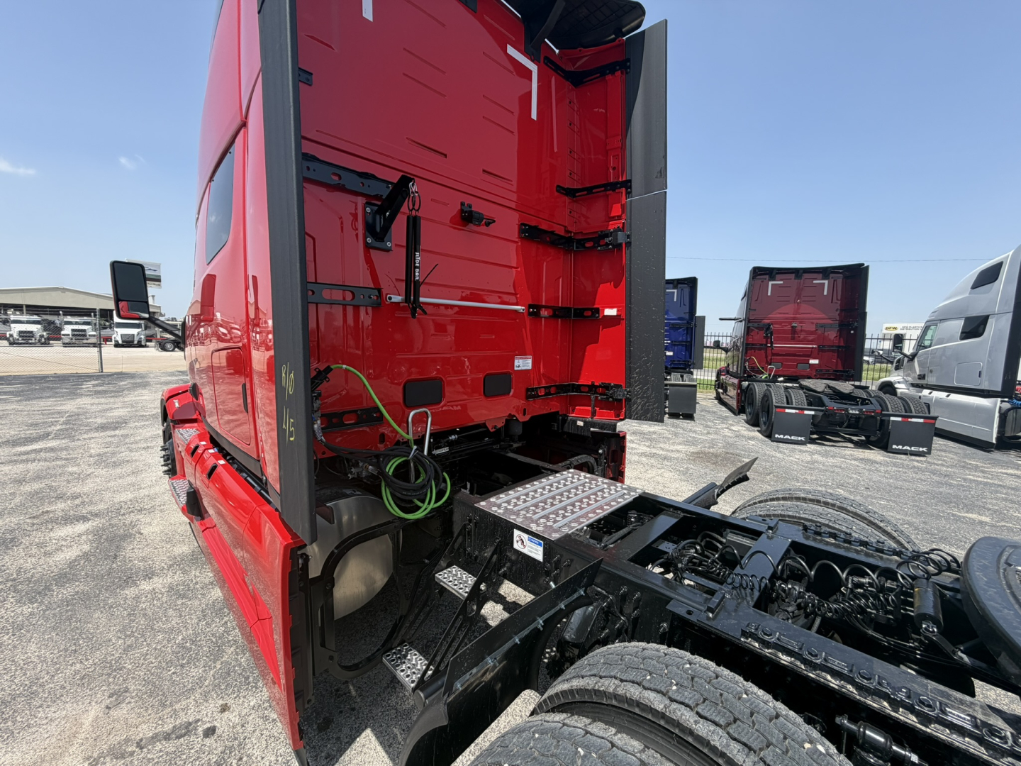 Mack PR64T76H tractor cab rear and chassis view showing side steps, fuel/water lines, and fifth-wheel area with red cab and black frame.