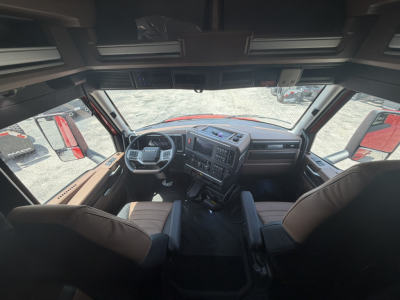 Interior cab of a new Mack PR64T76H truck showing steering wheel, dashboard with controls, two front seats, and large windshield.