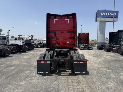 Truck chassis and rear view of a red cab on a Mack PR64T76H, with a clear view of the fifth wheel, dual rear axles, and Mack mud flaps in a dealership lot.