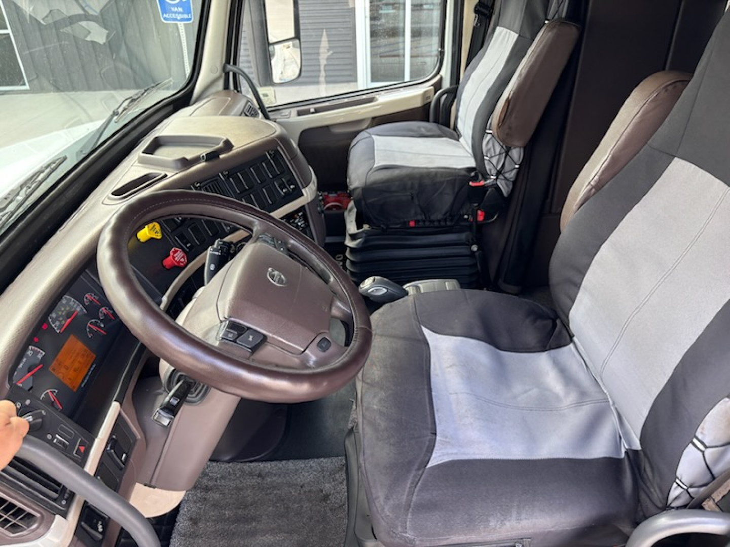 Volvo VNL780 cab interior showing steering wheel, dashboard, driver seat and passenger seat with two-tone fabric covers.