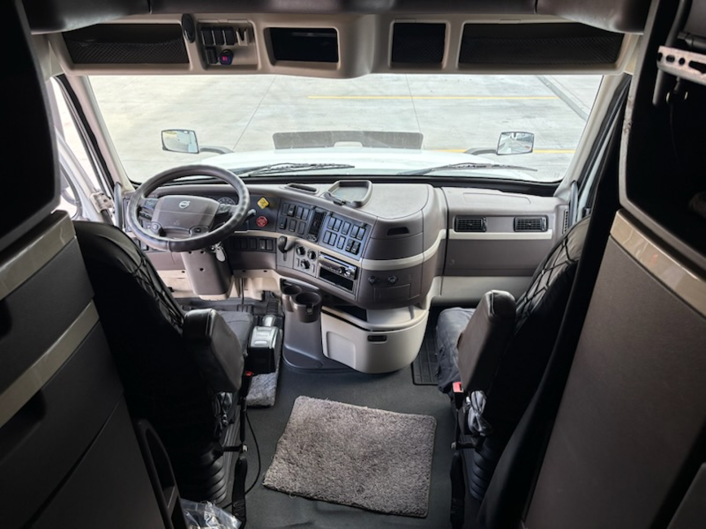 Volvo VNL780 truck cockpit interior showing steering wheel, dashboard with control panel and overhead storage, driver and passenger seats, windshield view.
