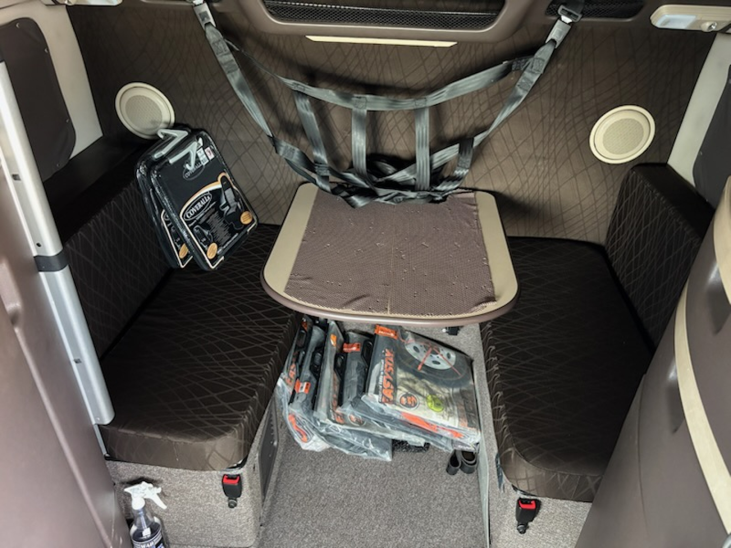 Volvo VNL780 sleeper cab interior with seating and storage; visible items include a small black toolbox or bag, a folded brown mat, and packs of tools or manuals under a center table.