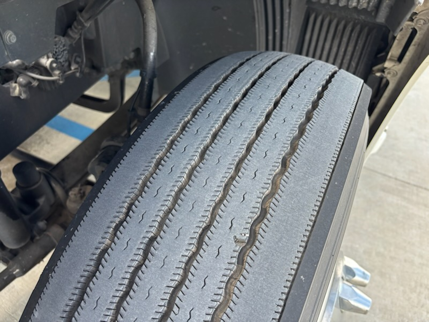Truck front wheel/tire close-up showing tread and sidewall on a Volvo VNL780 cab-over wheel area; visible components include suspension and undercarriage parts.