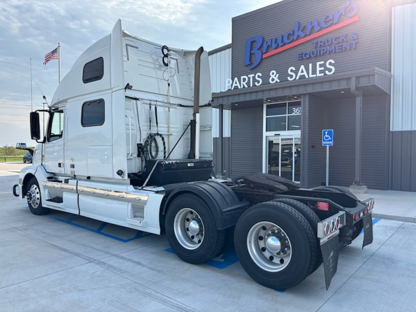 Truck rear/side view of a 2016 Volvo VNL780 sleeper tractor in a dealership lot showing the tractor’s white cab, dual rear axles, and fifth wheel with Brackney’s Parts & Sales building in background.
