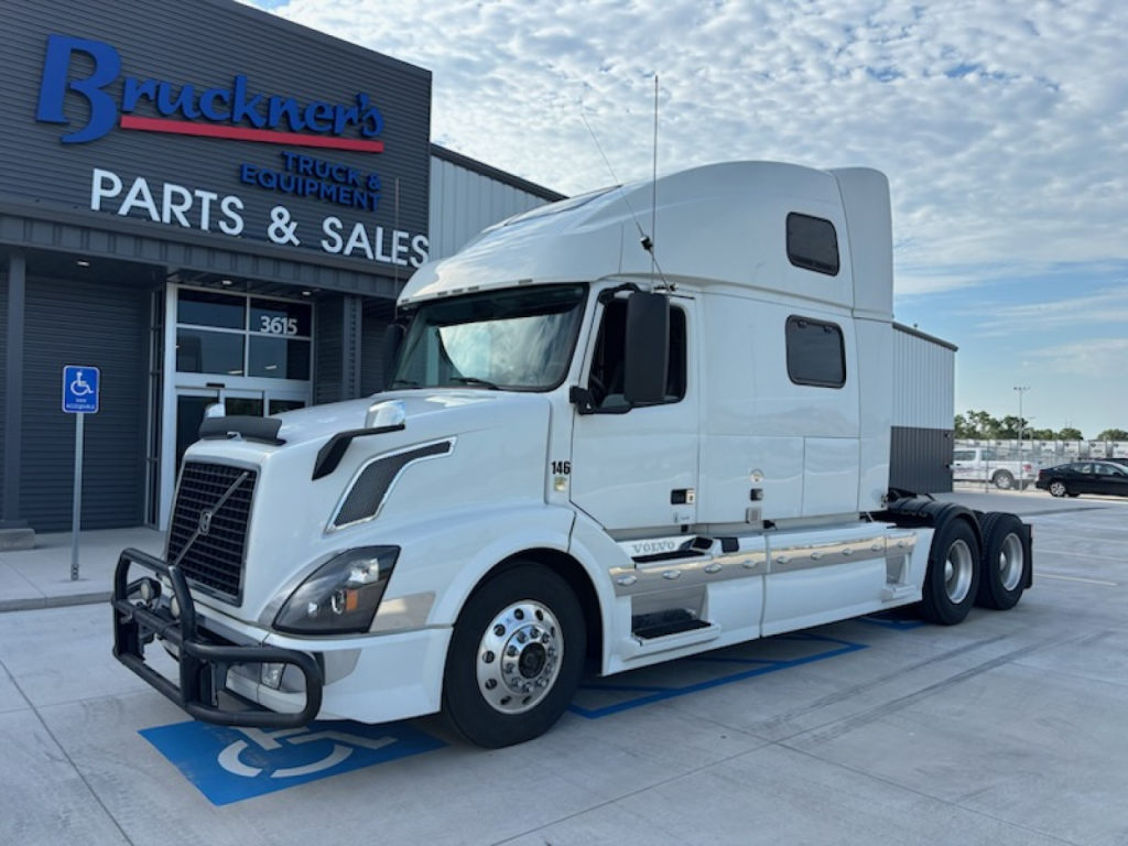 Volvo VNL780 truck in white, sleeper cab, front view parked at dealer lot with ‘Parts & Sales’ building in background.