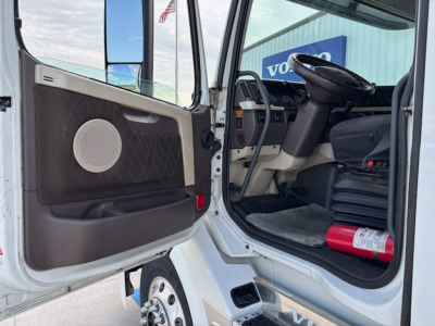 Truck cab interior of a 2016 Volvo VNL780 showing open driver door, steering wheel, dashboard, and a fire extinguisher on the floor.