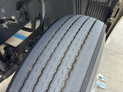 Truck front wheel/tire close-up showing tread and sidewall on a Volvo VNL780 cab-over wheel area; visible components include suspension and undercarriage parts.