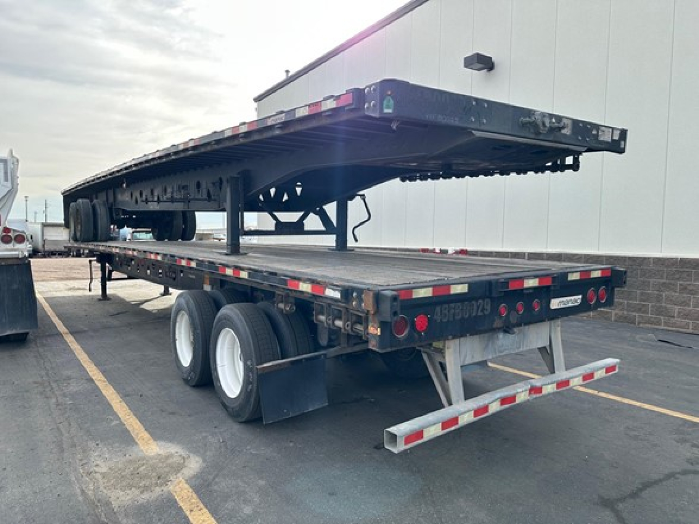 Flatbed trailer in service view showing steel flatbed and tandem axle with multiple wheels and rear underride bumper.