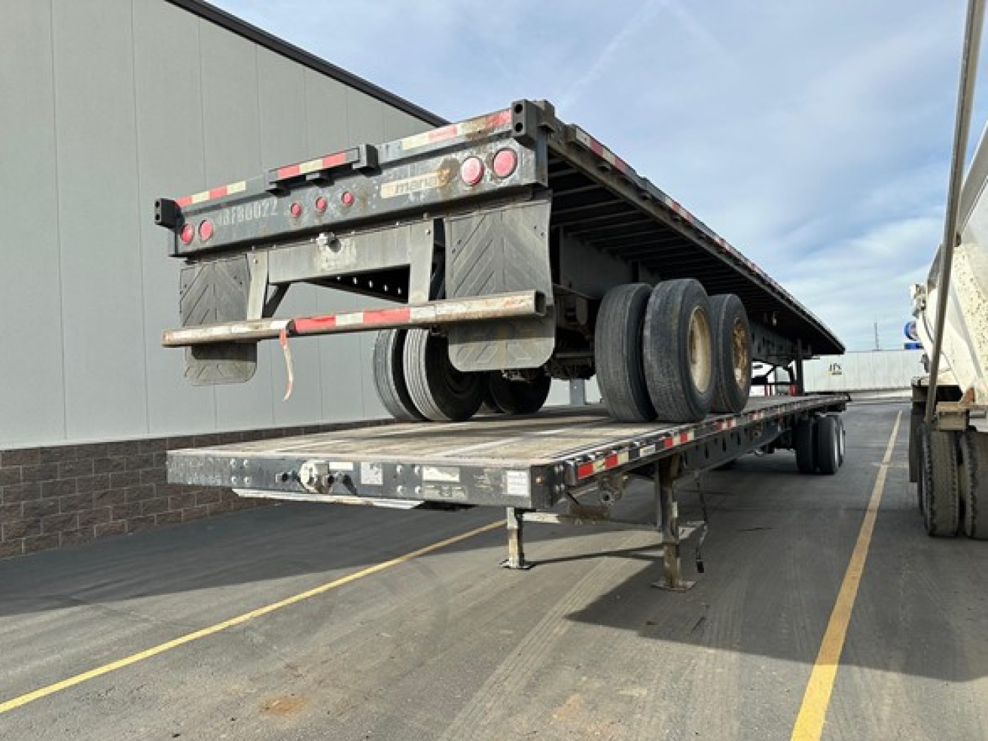 Trailer rear with flatbed and dual tandem axles showing license lights, reflectors, and bumper; side rails and support legs visible.