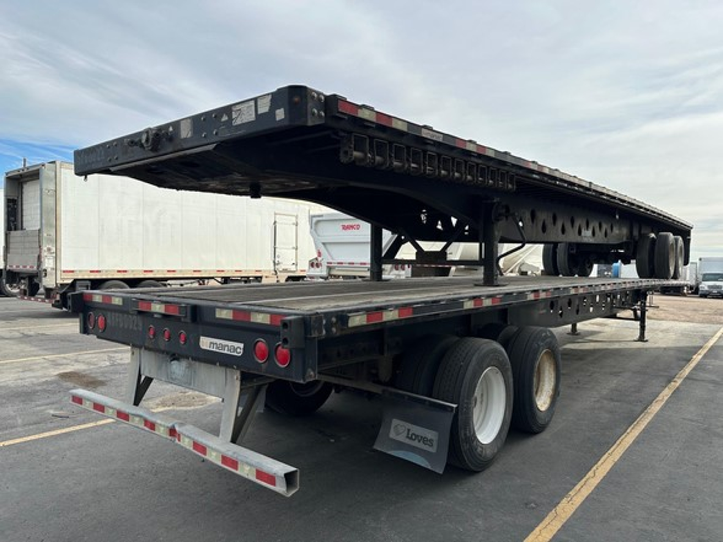 Manac steel flatbed trailer in-service showing open deck with multiple axles and rear bumper lights.