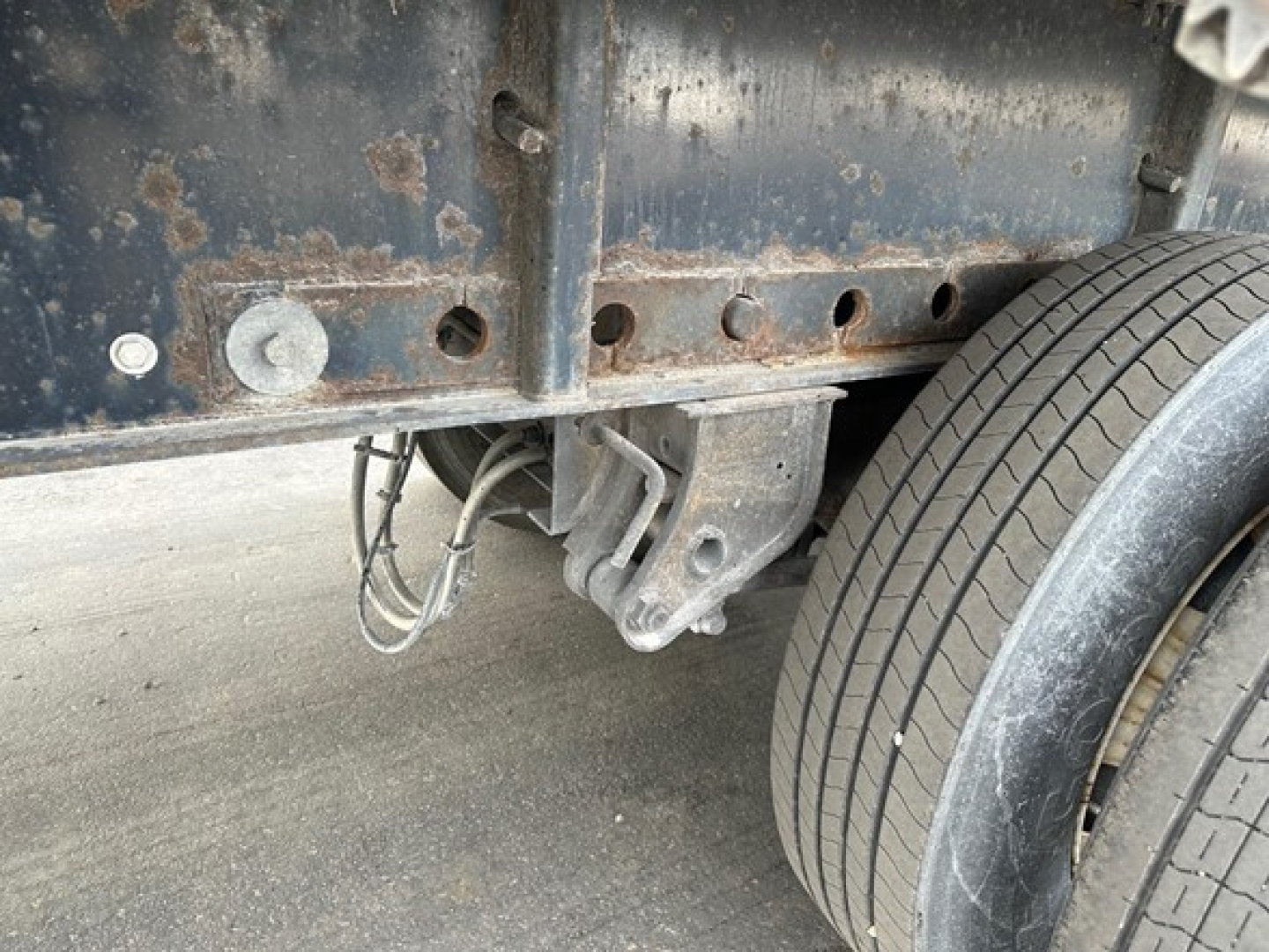 Trailer hitch area of a 2015 Manac steel flatbed showing undercarriage with mounting bracket and dual rear tires.